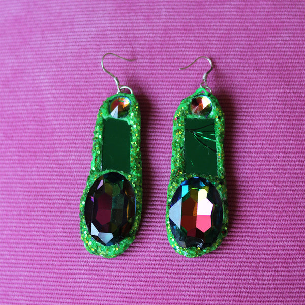 Green glittery earrings with multicolored gemstones on a pink background
